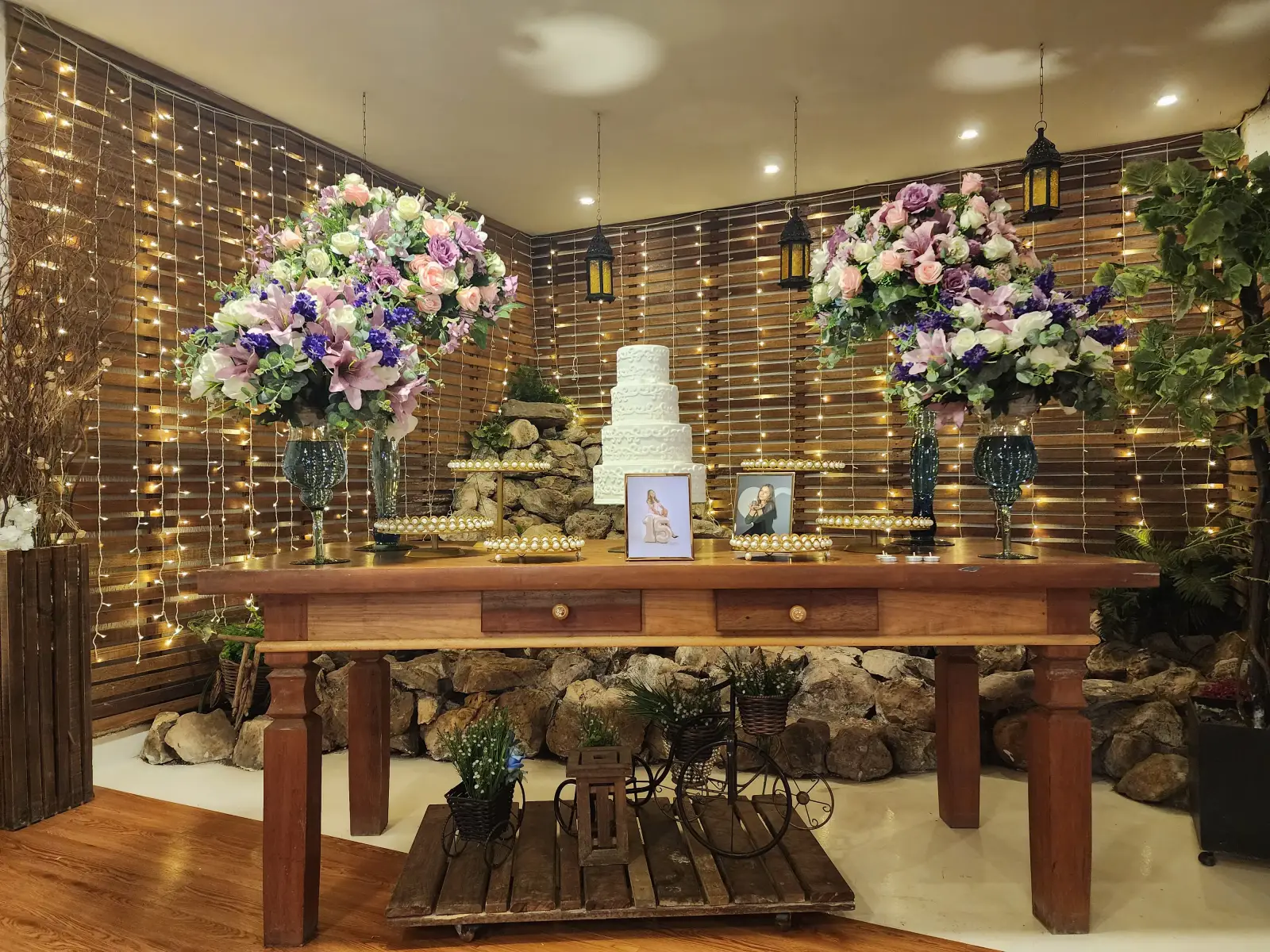 Mesa de debutante com arranjos lilás e parede de luzes