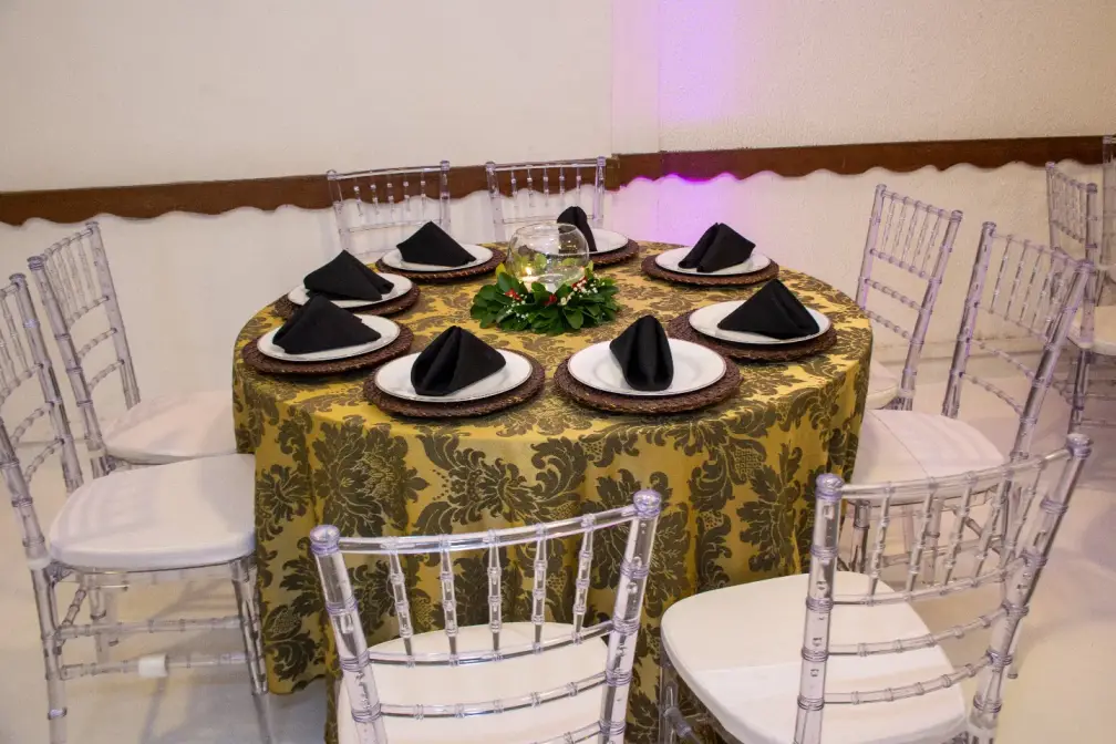 Mesa posta com toalha dourada, cadeiras Tiffany e guardanapos pretos